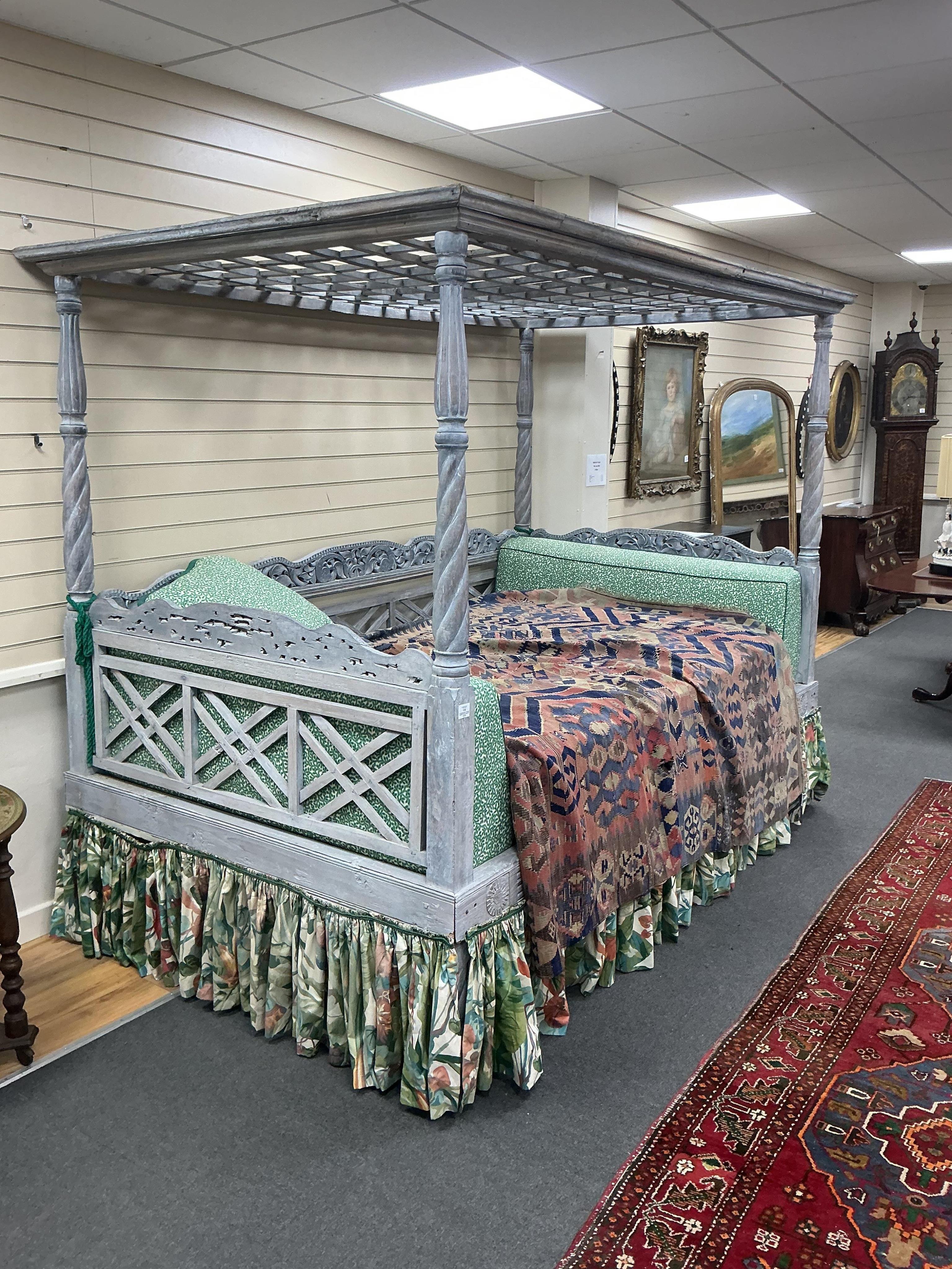 An Indian grey painted carved teak four poster double bedstead, with a pierced canopy over